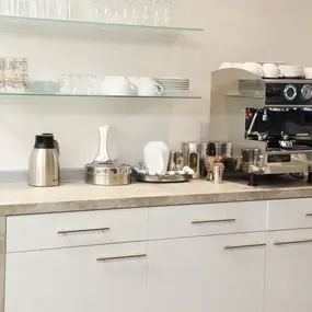 Moderne Kaffeeküche mit Espressomaschine, Tassen, Gläsern, Thermoskanne und Geschirr.